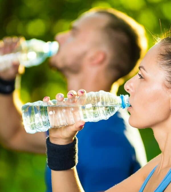 A man and woman are drinking water in a park.