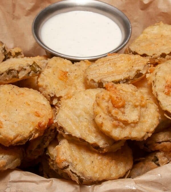 Fried pickles in a brown paper bag with dipping sauce.