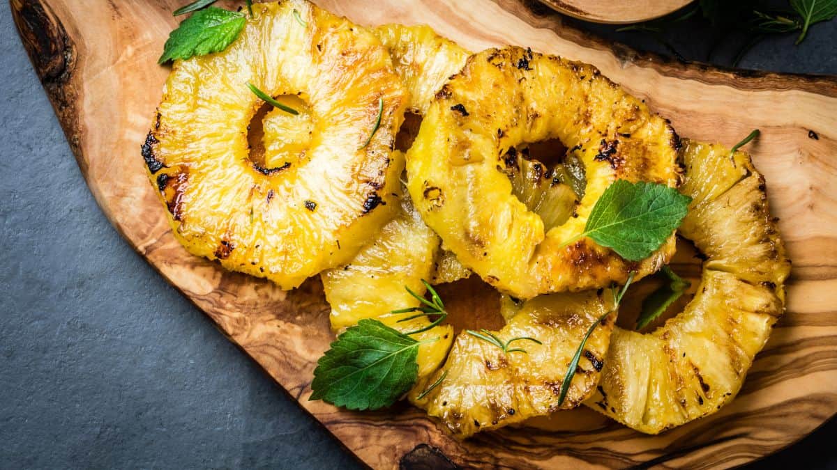 Grilled pineapple slices garnished with mint on a wooden serving board.