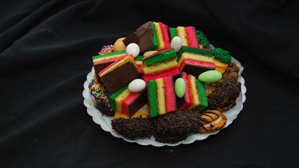 An assortment of colorful layered cakes and various chocolate-coated cookies on a plate.