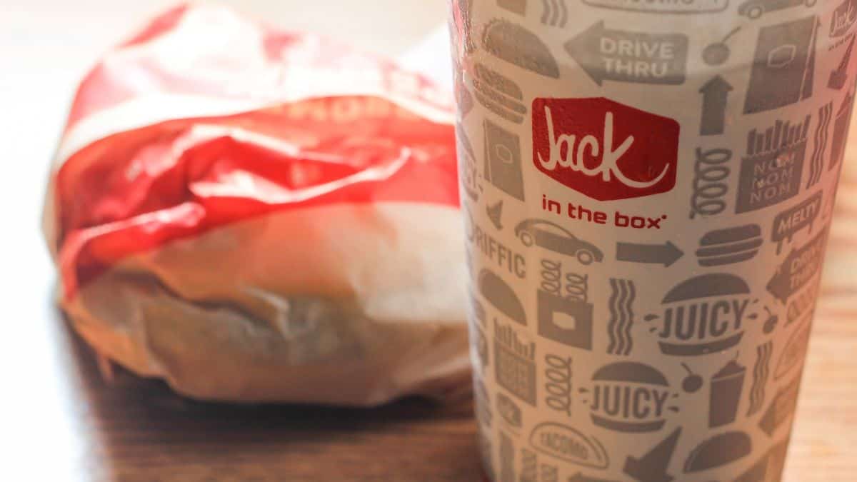A jack in the box fast food cup with a wrapped sandwich in the background.