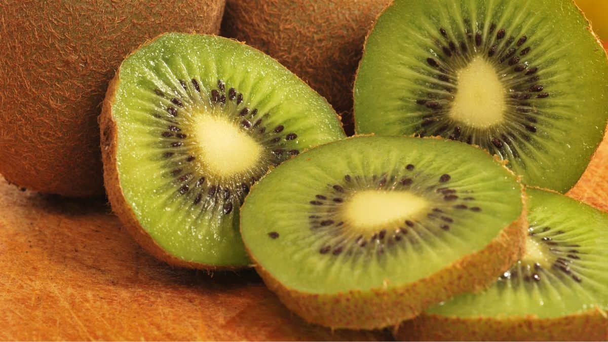 Sliced ripe kiwi fruit with one whole kiwi in the background.