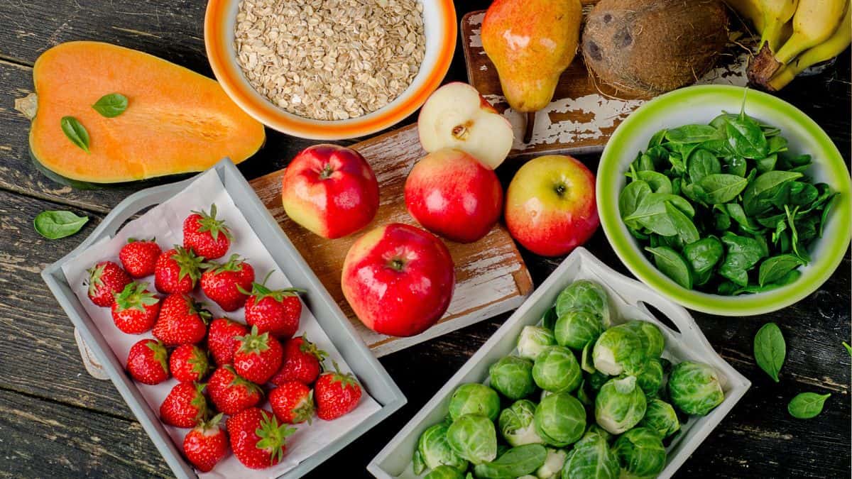 Assorted healthy foods, including fruits, vegetables, and oats, displayed on a wooden surface, are the worst foods to eat before bed.