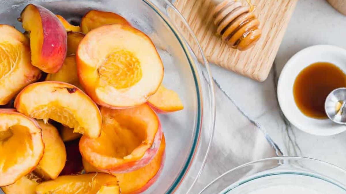 Sliced peaches in a glass bowl with a honey dipper and a small dish of honey on the side.