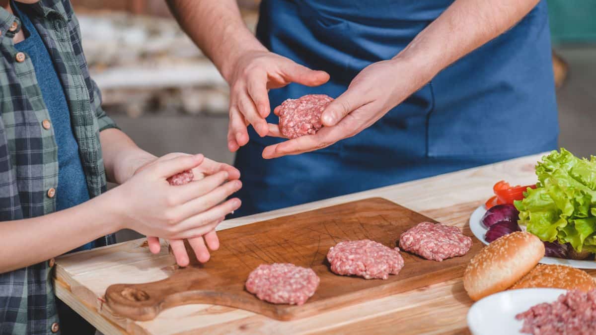 A man and a boy are preparing hamburgers on a cutting board.