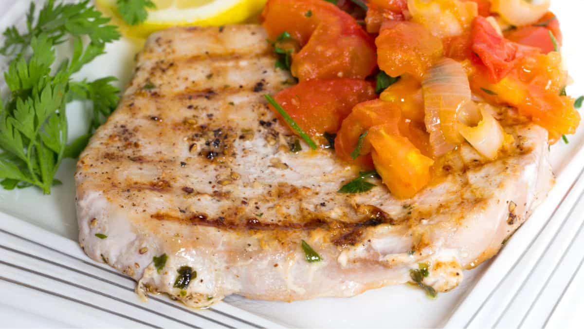 Grilled fish with tomatoes on a white plate.