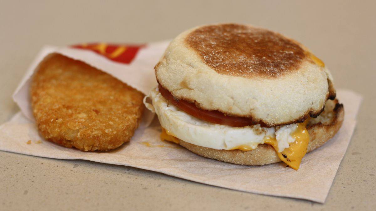 A breakfast sandwich with egg, cheese, and meat on an english muffin, accompanied by a hash brown.