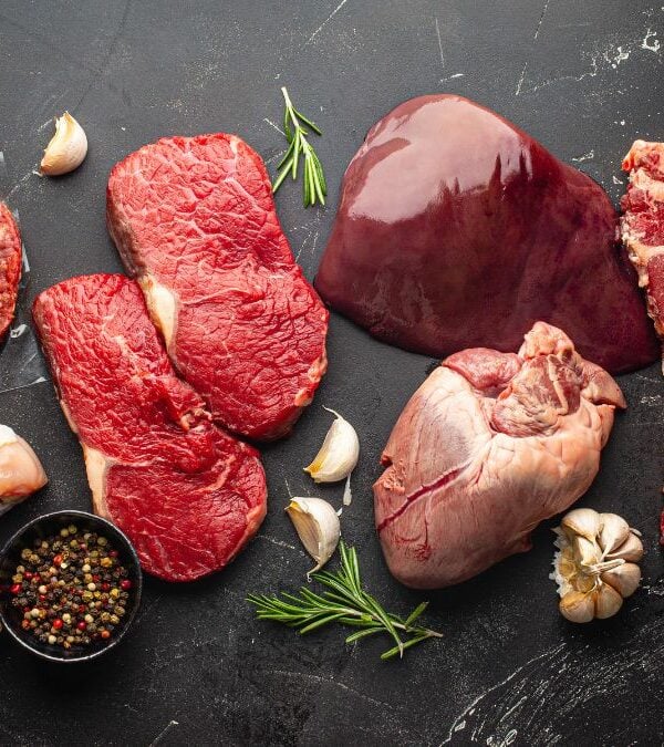 Various raw meats and poultry arranged with spices and herbs on a dark surface.