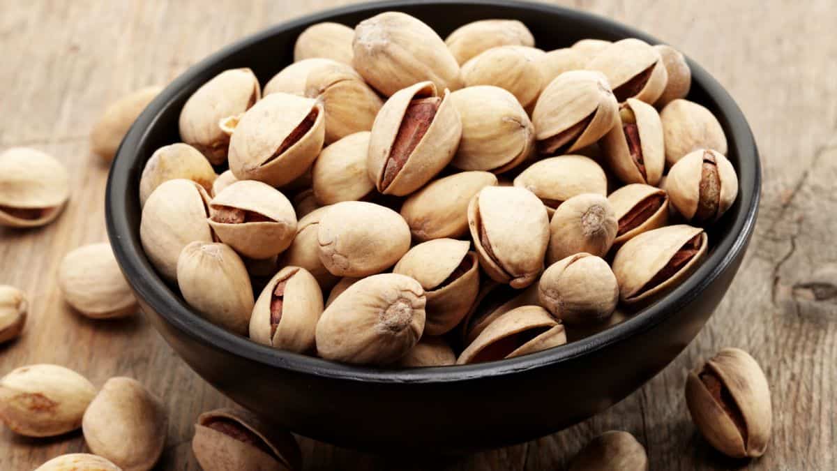 A bowl of pistachios, considered on a wooden surface.
