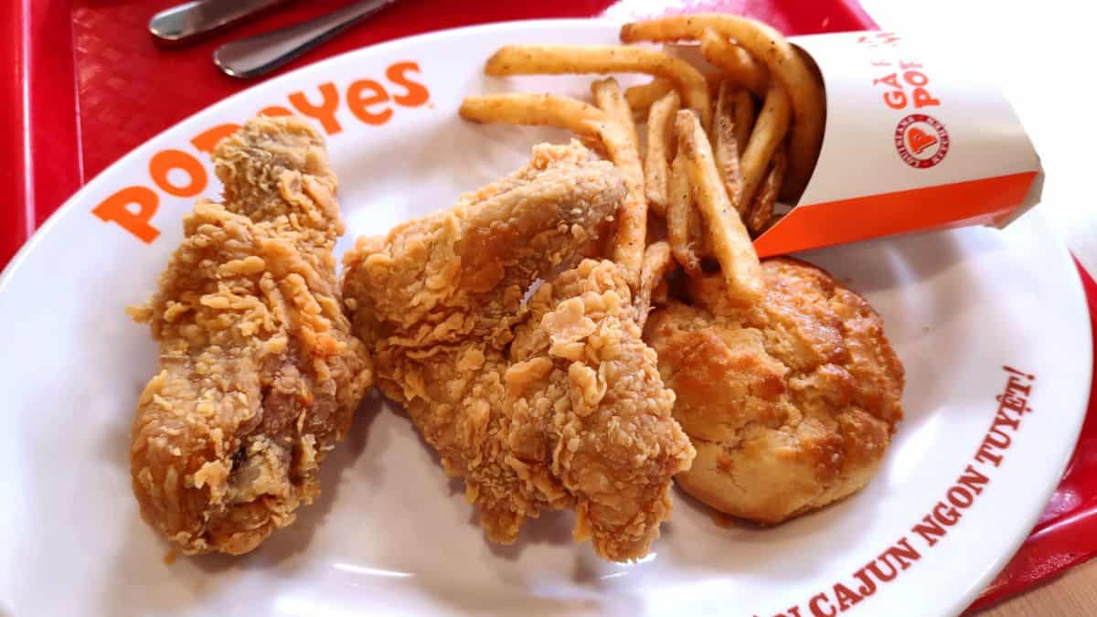 Fried chicken pieces with fries and a biscuit served on a white plate, with a popeyes logo visible.