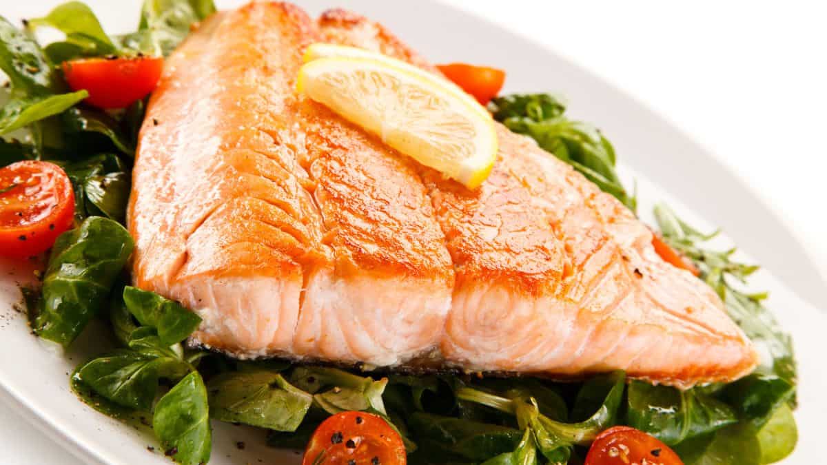 Grilled salmon fillet served on a bed of spinach with cherry tomatoes and a slice of lemon.