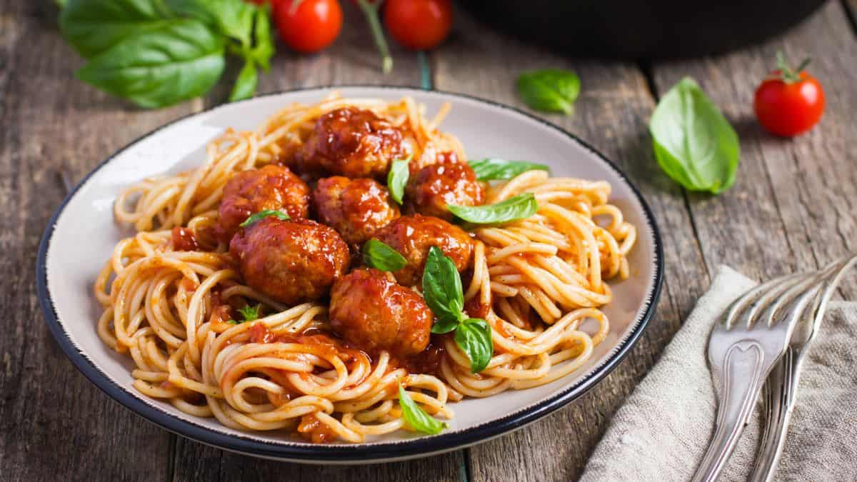 Plate of spaghetti with meatballs garnished with basil leaves.