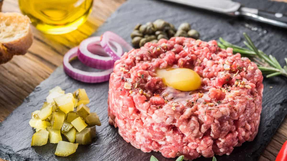 Classic steak tartare with a raw egg yolk, capers, pickles, and onions, served on a slate board.
