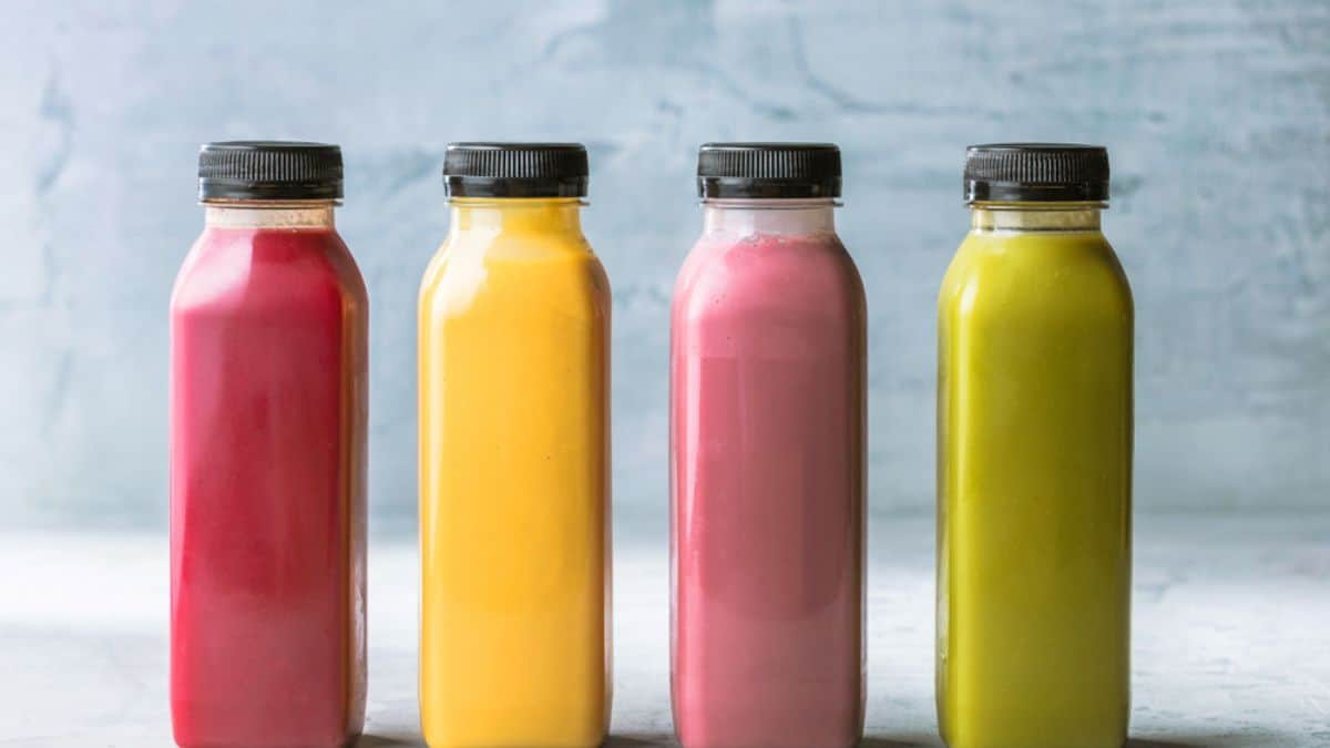 Four bottles of colorful smoothies in a row against a light background.