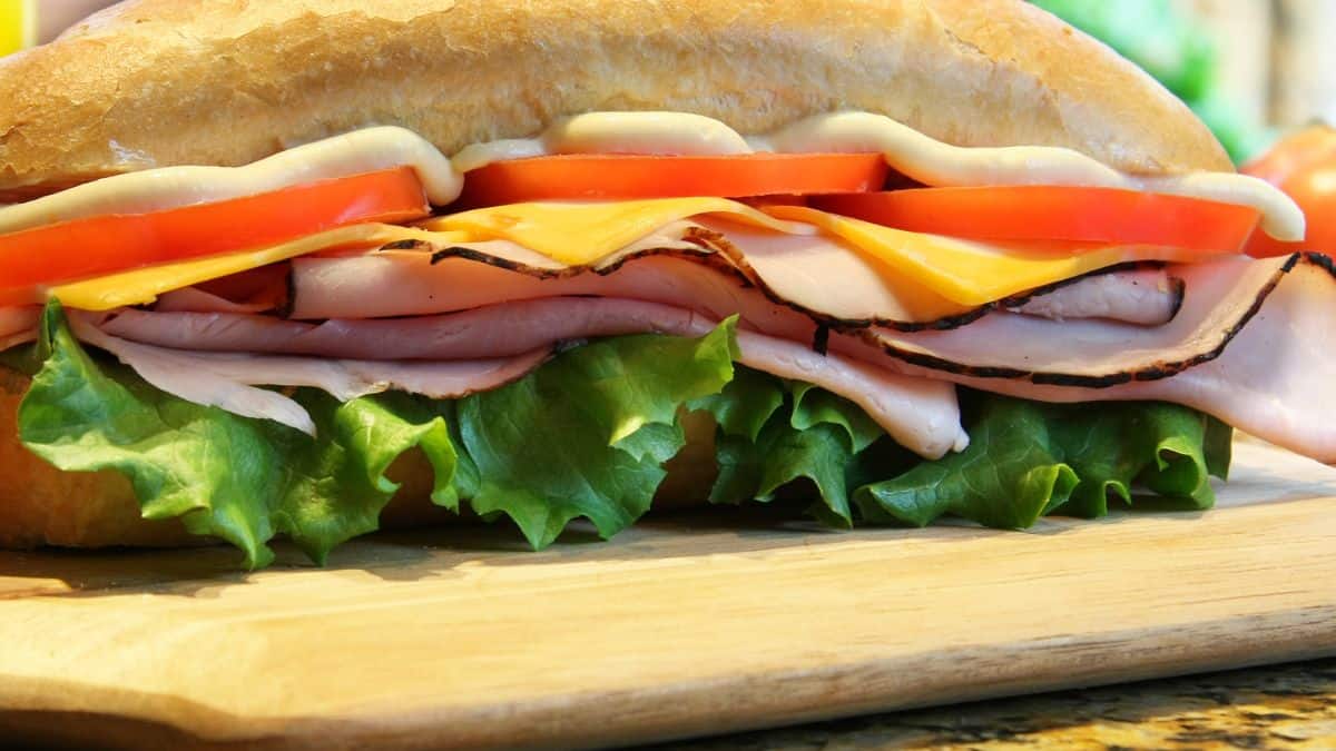 A close-up of a turkey sandwich with lettuce, tomatoes, cheese, and mayonnaise on a wooden cutting board.