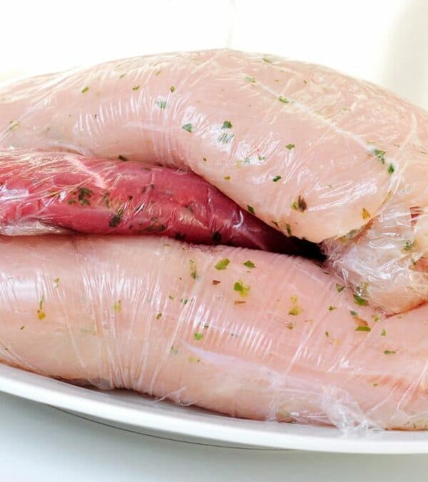Two pieces of meat wrapped in plastic on a plate.