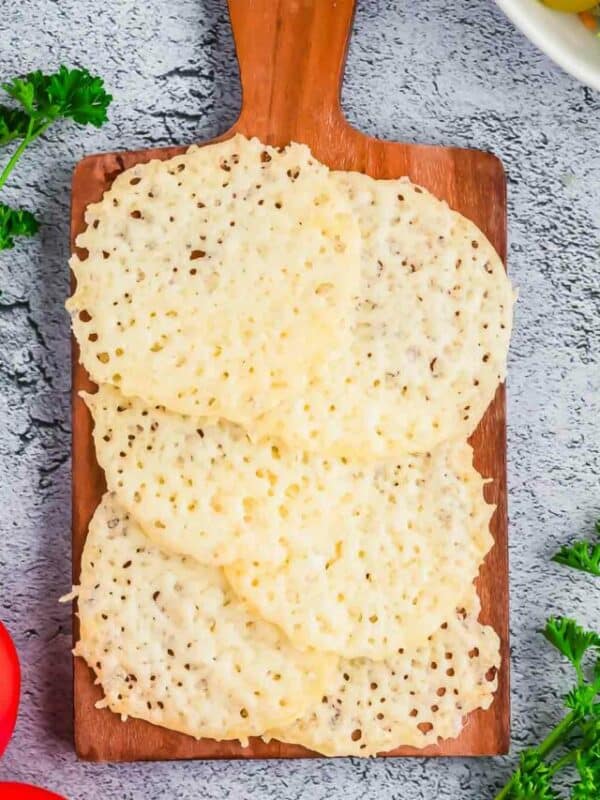 A wooden cutting board with cheese, tomatoes and parsley.