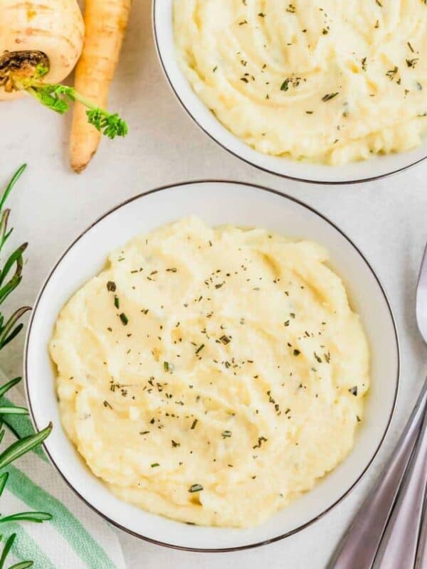 Bowl of creamy mashed potatoes garnished with herbs on a table.