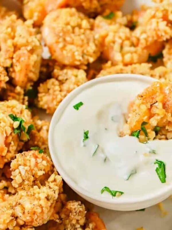 Breaded shrimp served with a side of creamy dipping sauce, garnished with chopped herbs.