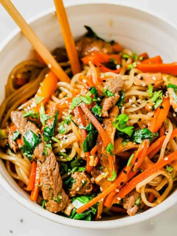 A bowl of asian beef noodles with carrots and chopsticks.