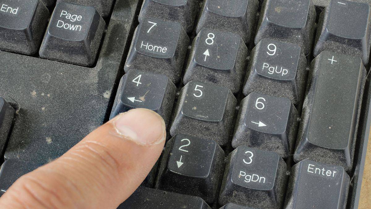 A finger pressing the number 5 key on a dusty computer keyboard.