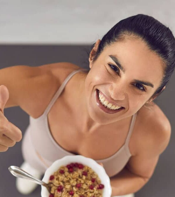 A woman giving a thumbs up with a bowl of cereal.