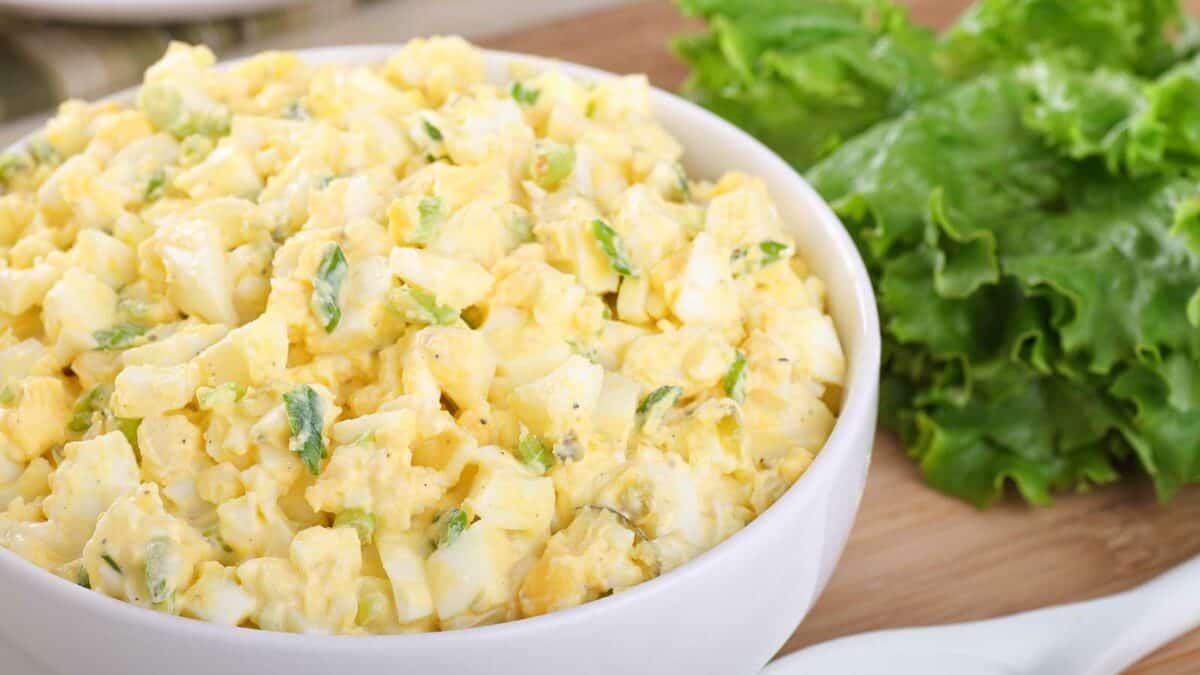 Bowl of creamy potato salad garnished with herbs next to fresh lettuce leaves.