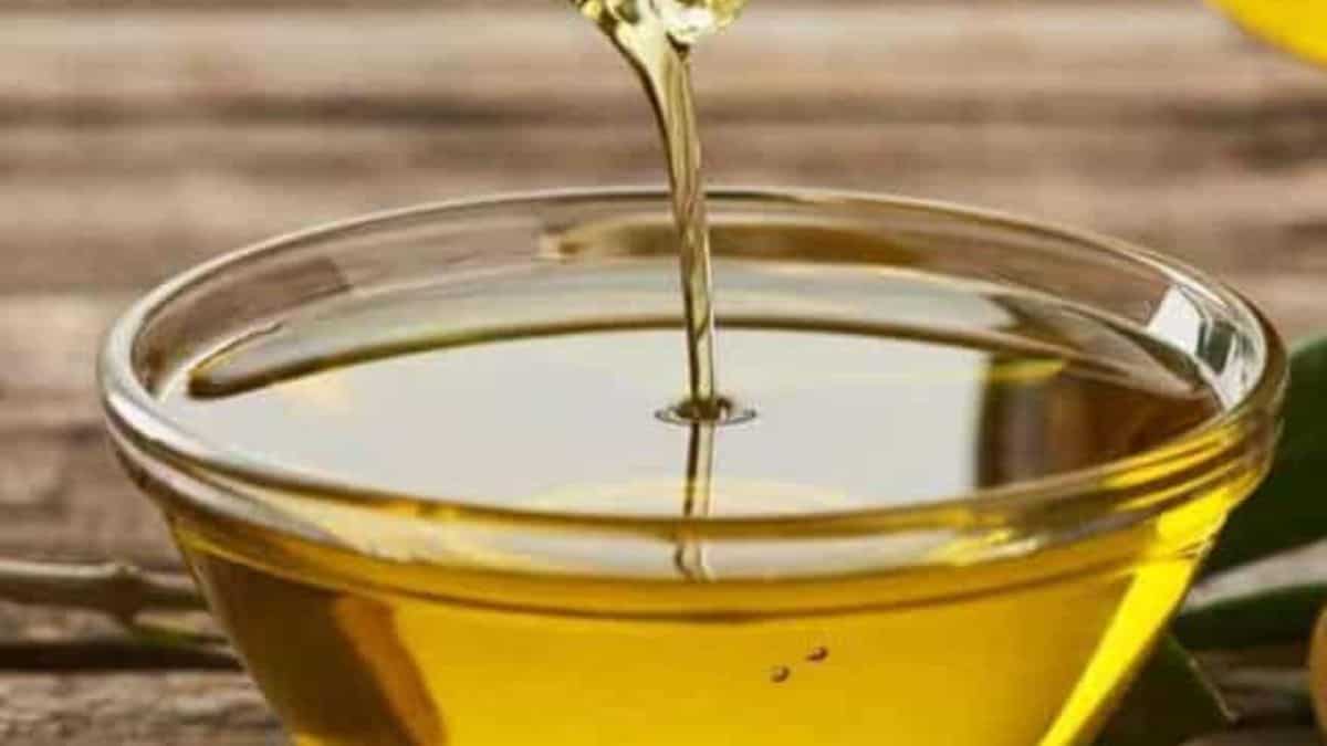 Golden liquid, likely oil, being poured into a glass bowl on a wooden surface.