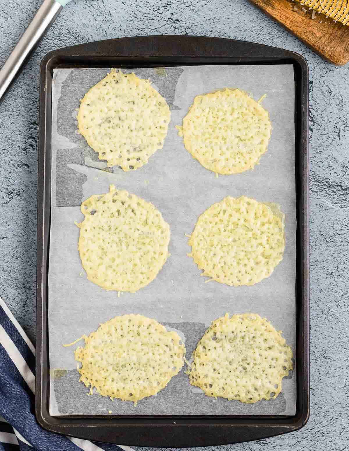 A baking sheet lined with parchment paper and baked parmesan crisp circles on it.