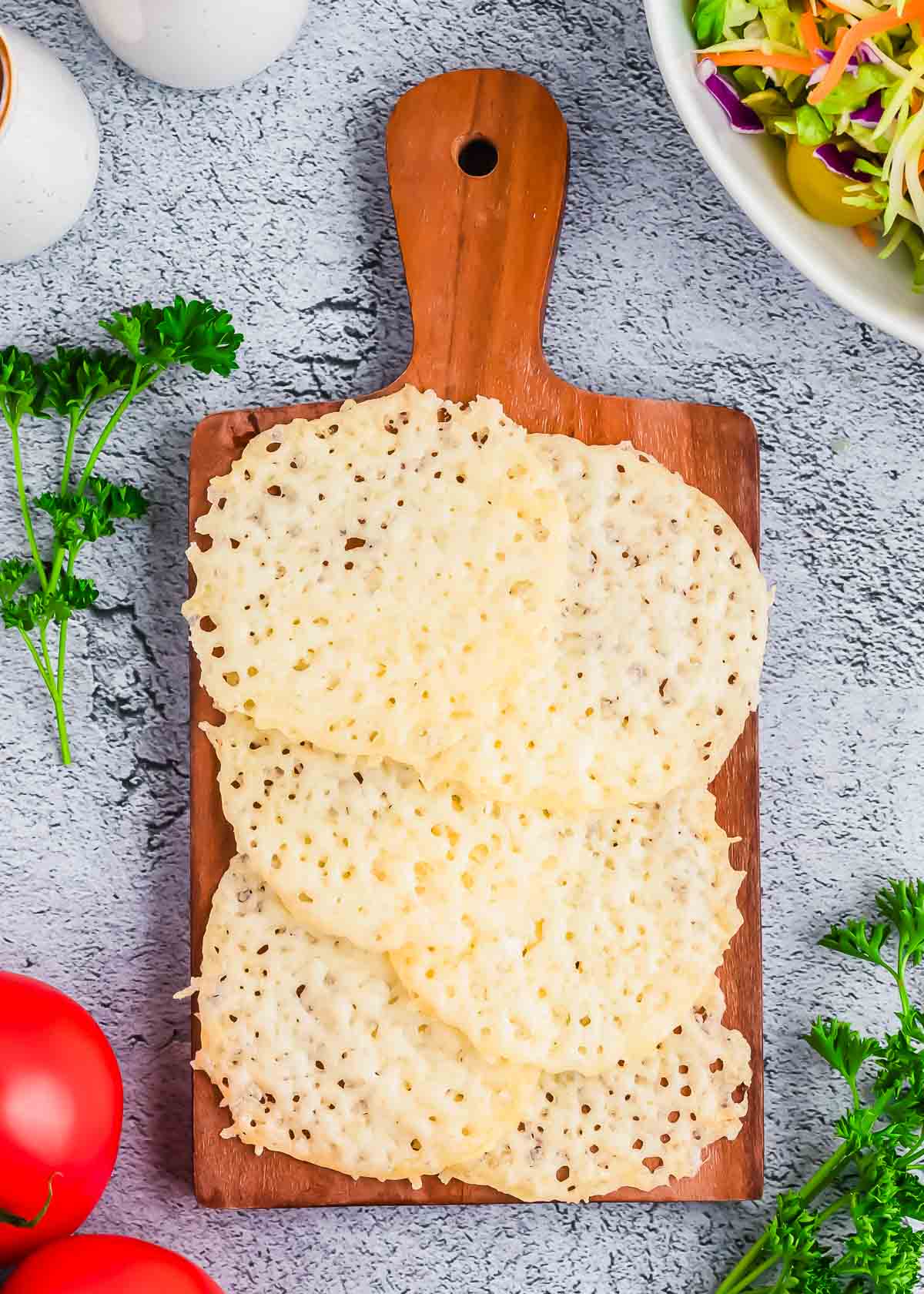 A wooden cutting board with cheese crisps stacked on top.