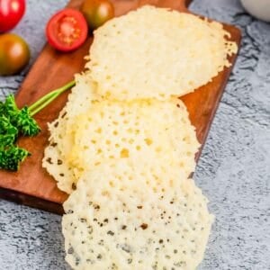 Parmesan crisps arranged on a wooden cutting board.