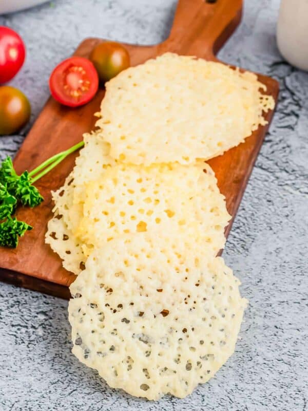 Parmesan crisps arranged on a wooden cutting board.