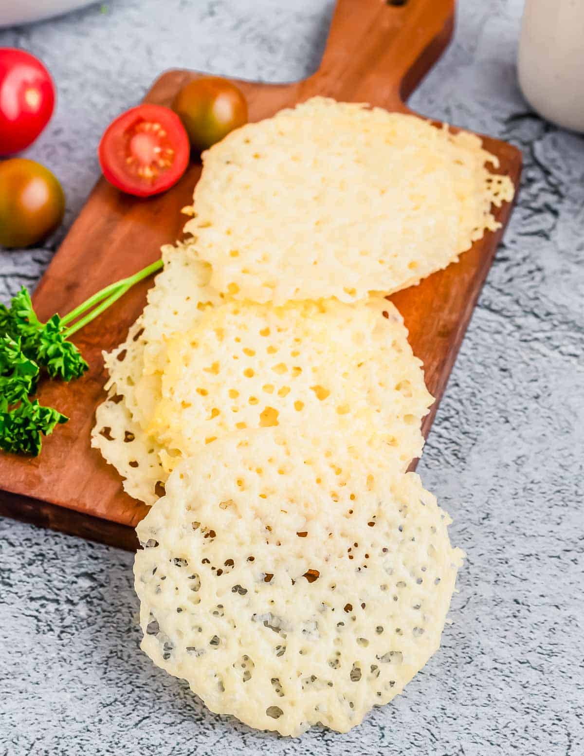 Parmesan crisps arranged on a wooden cutting board.