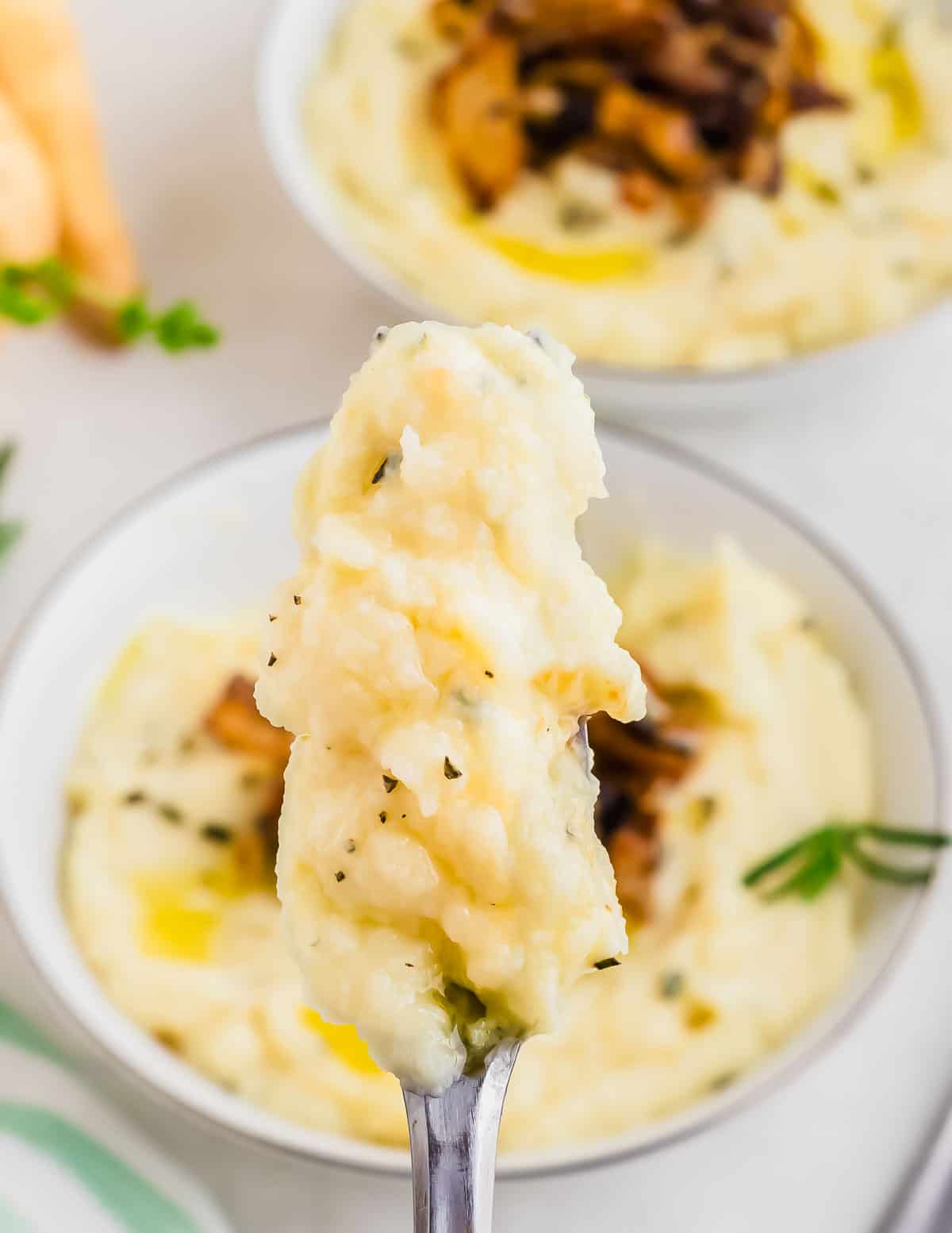 A spoonful of creamy parsnip puree with herbs, with a bigger bowl in the background.