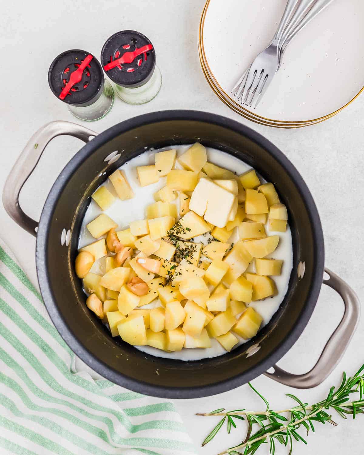 Chopped cooked parsnips in a pot with milk, rosemary, butter and roasted garlic ready to be mashed.