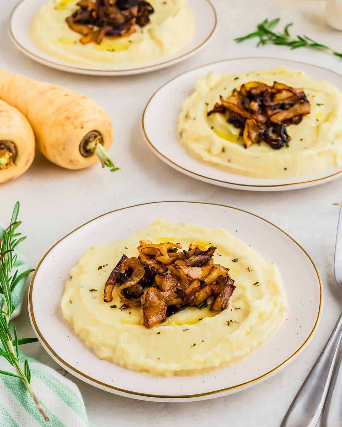 Parsnip puree topped with caramelized onions on a white plate, garnished with fresh herbs.