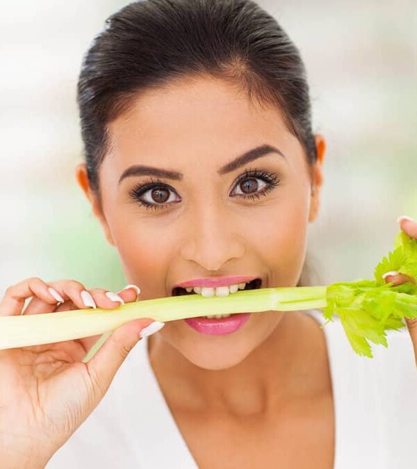 Woman playfully biting a stick of celery.