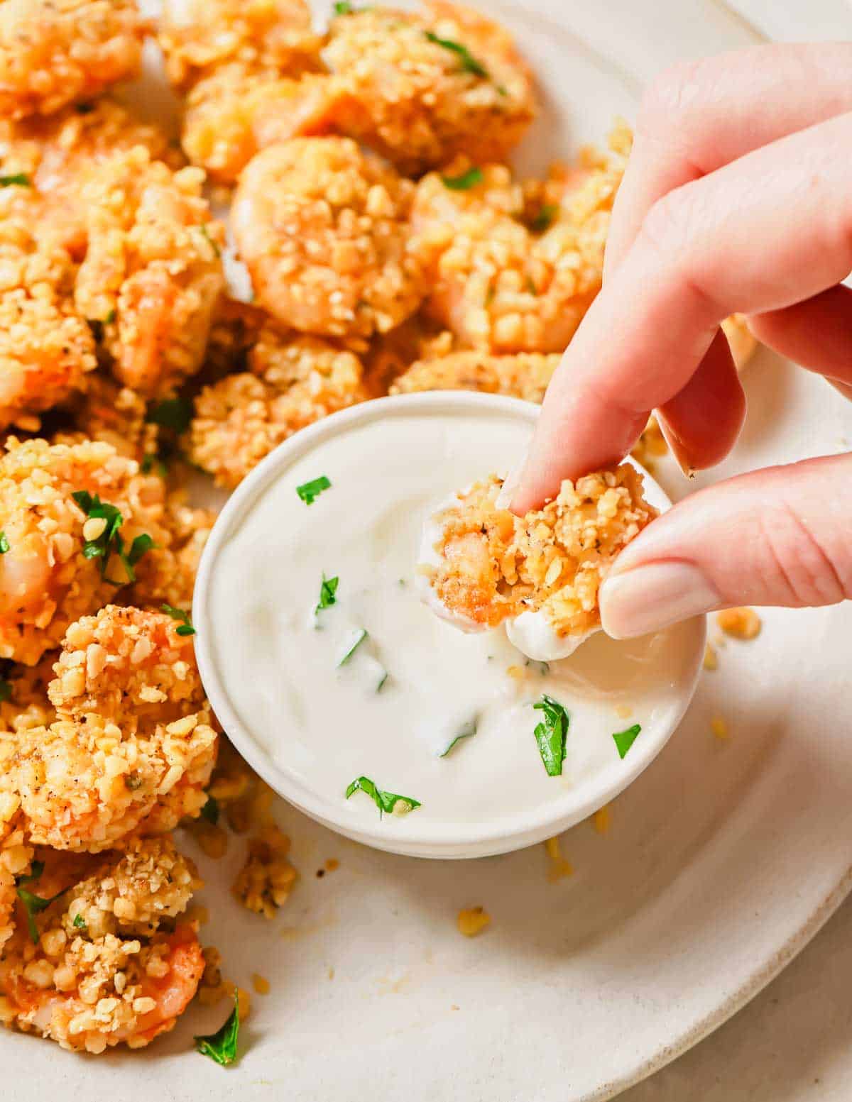 A person's hand dipping a piece of popcorn shrimp into a white sauce.