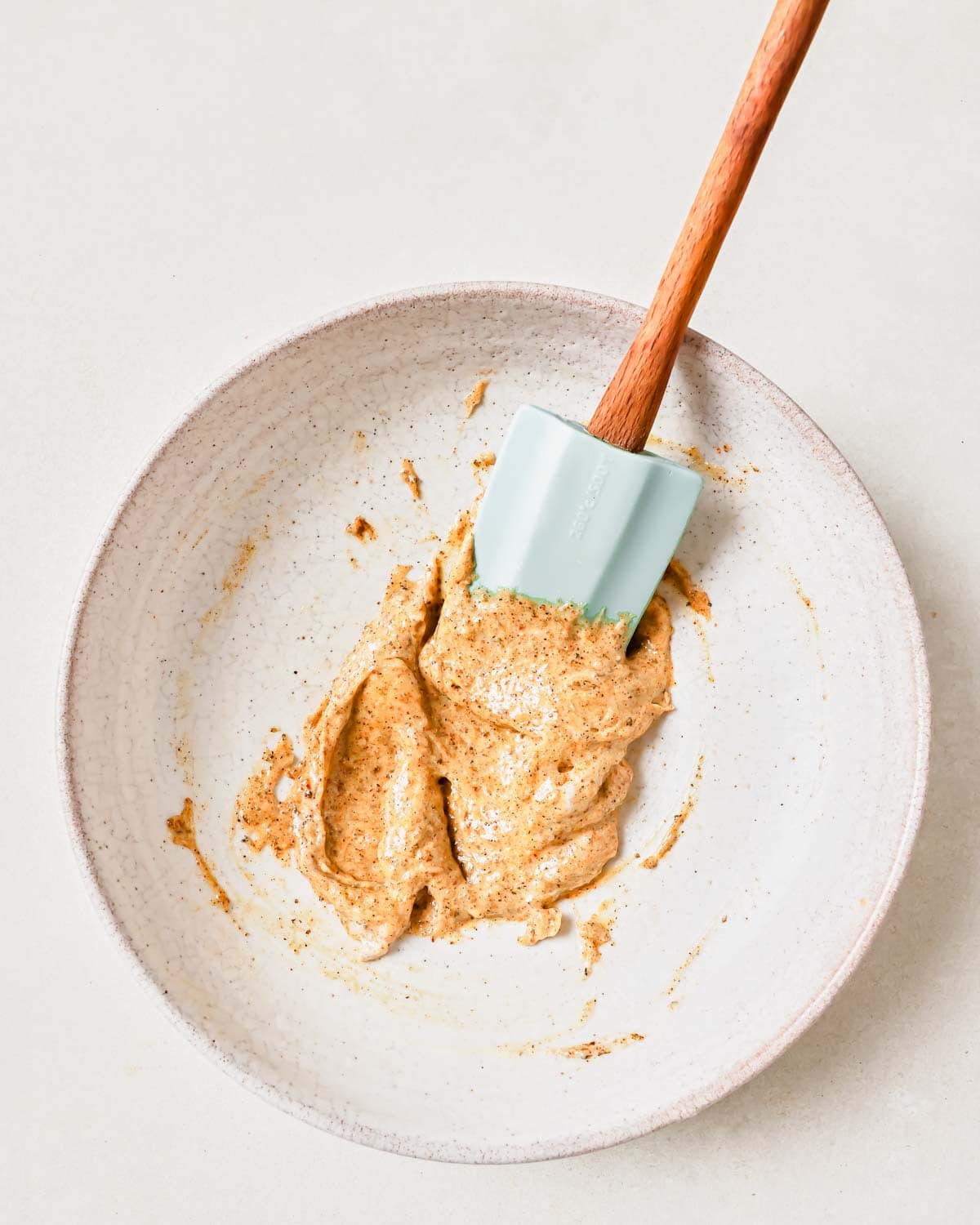 Seasoning spices and mayonnaise mixed together in a bowl with a wooden spoon.