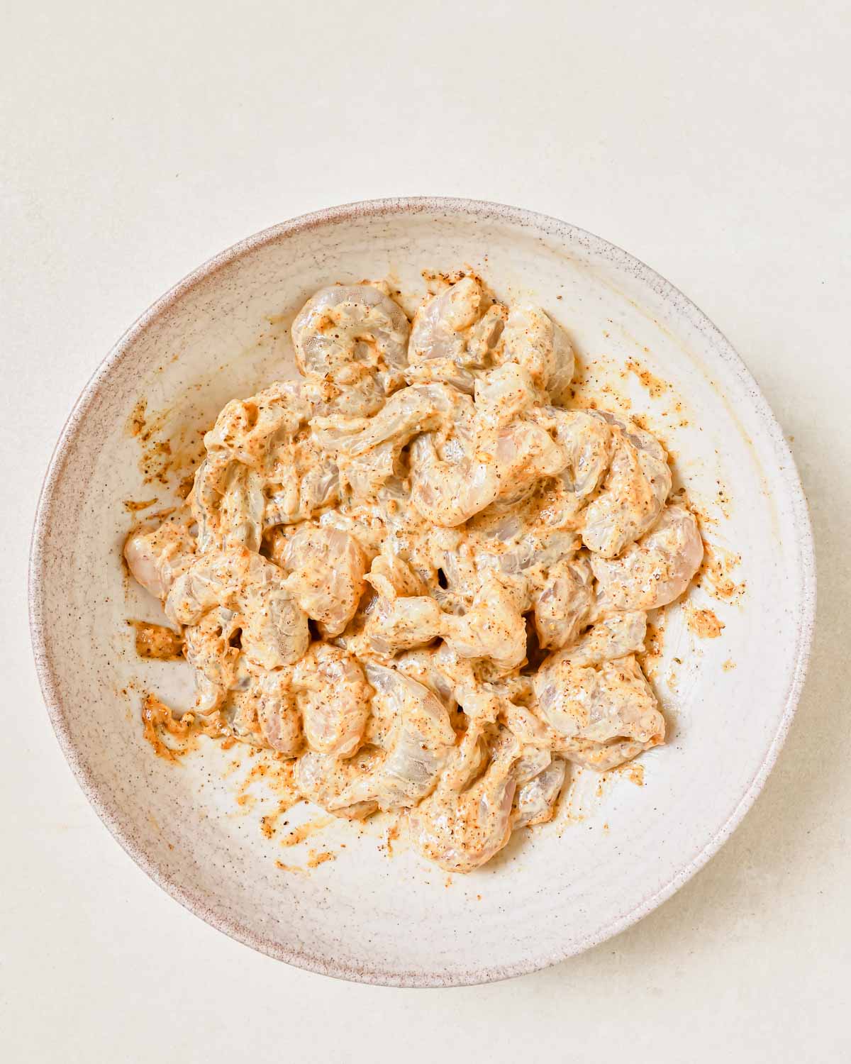 A bowl of shrimp coated in a mayo mustard sauce in a white bowl on a white surface.