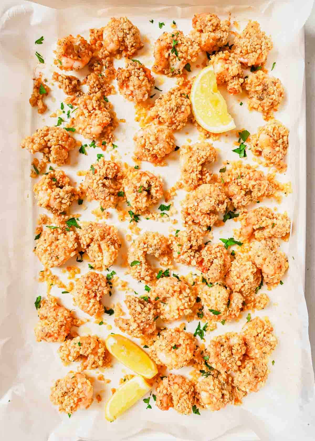 Baked popcorn shrimp on a baking sheet with lemon wedges.