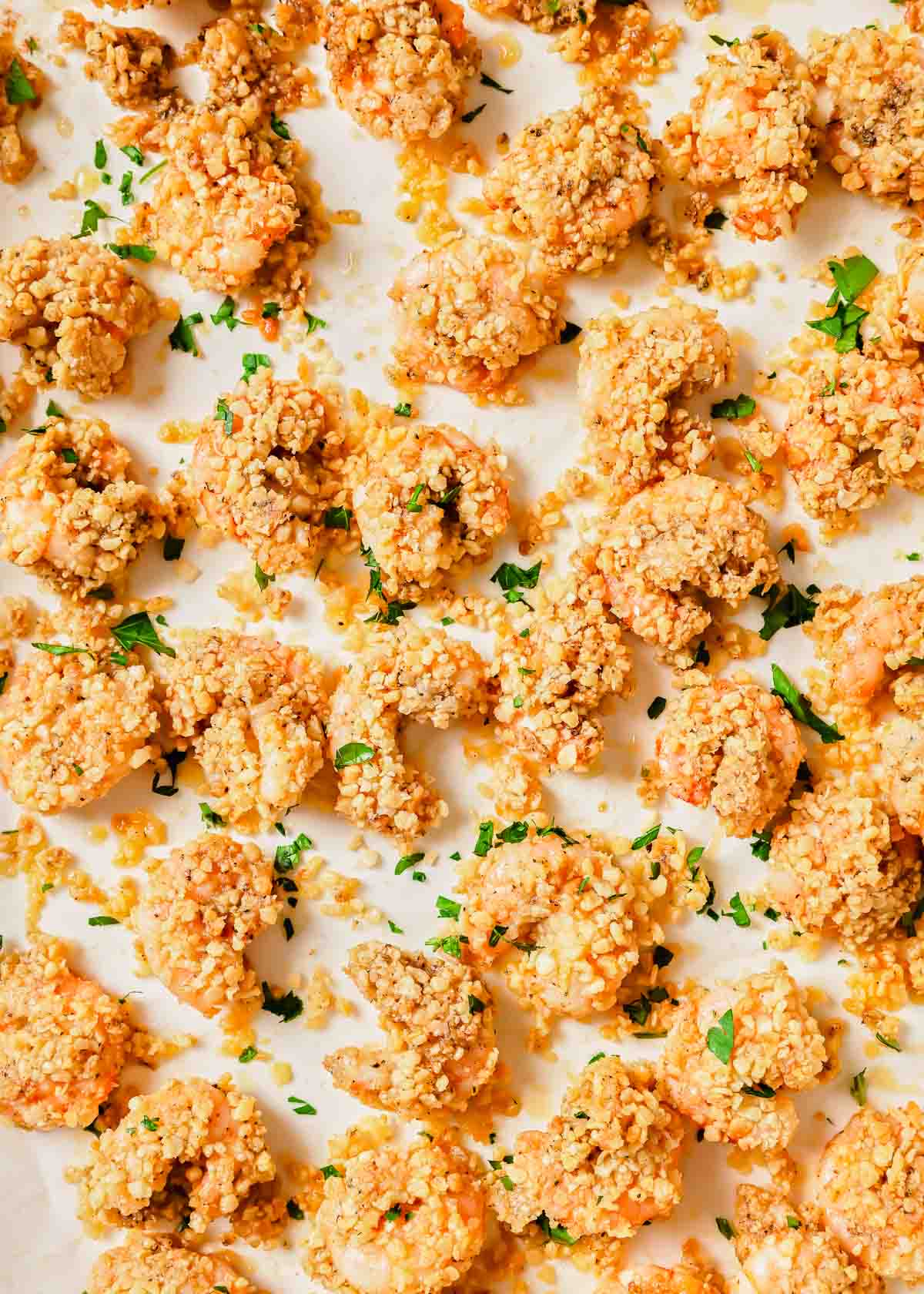 A baking sheet of oven-baked popcorn shrimp garnished with parsley.