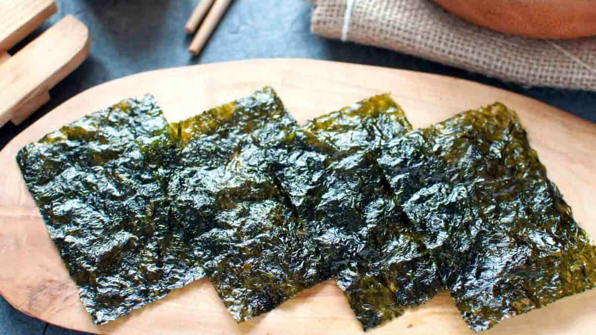 Roasted seaweed sheets on a wooden board with chopsticks in the background.