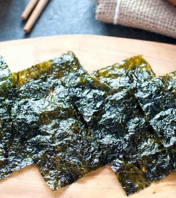 Roasted seaweed sheets on a wooden board with chopsticks in the background.