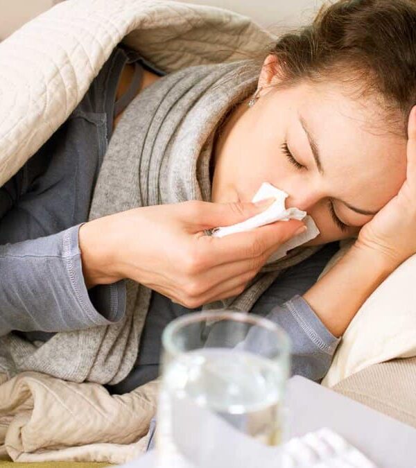 A woman resting on a couch appears to be ill, holding a tissue to her nose.