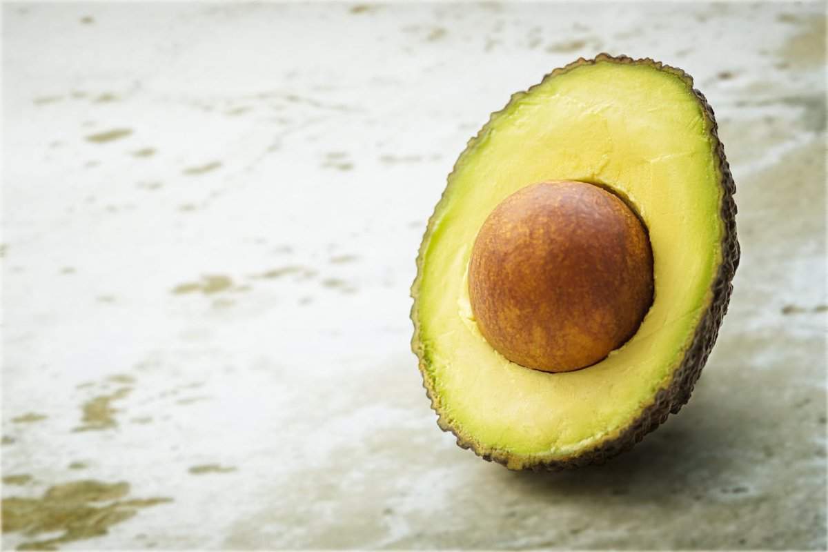 A halved Hass avocado with its pit on a textured surface.