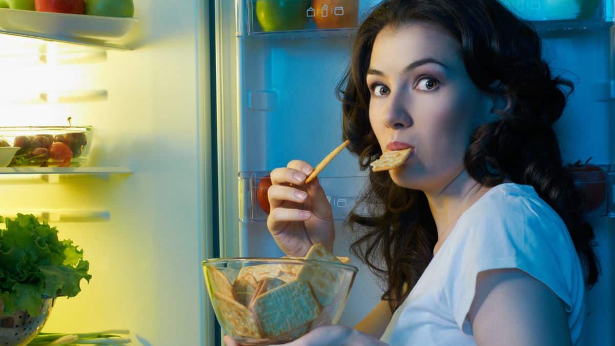Woman eating a snack by the fridge at night.