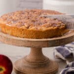 Slicing a freshly baked apple cake on a wooden cake stand.