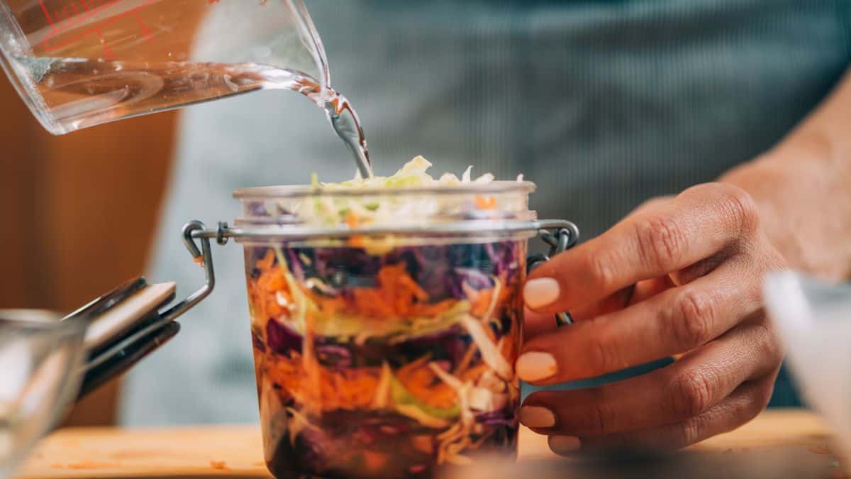 Person pouring liquid dressing into a jar of layered salad.