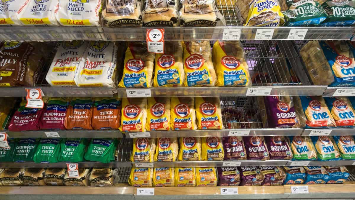 Shelves stocked with various brands and types of sliced bread in a grocery store.